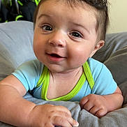 Zavier is registered to the contest to win money with this photo: baby, child, infant, face, smile, curly_hair, blue_clothing, green_trim, hand, cushion, soft, indoors, portrait, cute, happy, skin, eyes, expression, person, young