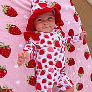 Maeve joined the competition — help win amazing prizes! baby, infant, strawberry_pattern, hat, onesie, pink_blanket, patterned_clothing, cute, child, outdoor, toddler, smiling, reaching_hand, fabric, playful, person, lying_down, soft_texture, colorful, happy