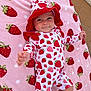 baby, infant, strawberry_pattern, hat, onesie, pink_blanket, patterned_clothing, cute, child, outdoor, toddler, smiling, reaching_hand, fabric, playful, person, lying_down, soft_texture, colorful, happy