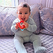 Issam a rejoint le concours — aidez-le/la à gagner de superbes lots ! baby, child, onesie, teething_ring, happy, smiling, sitting, bedspread, patterned, pillow, window, indoor, cozy, cute, infant, young_child, playful, soft_light, home, portrait