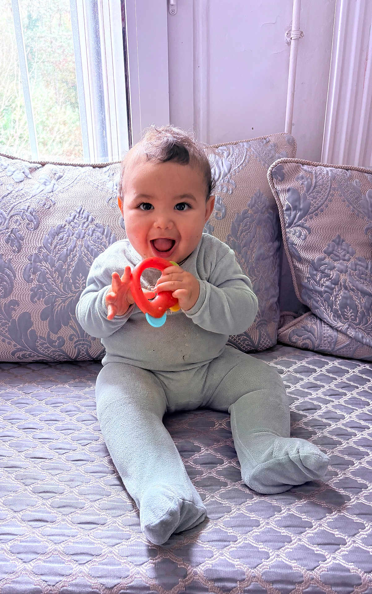 Issam a rejoint le concours — aidez-le/la à gagner de superbes lots ! baby, child, onesie, teething_ring, happy, smiling, sitting, bedspread, patterned, pillow, window, indoor, cozy, cute, infant, young_child, playful, soft_light, home, portrait