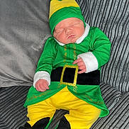 Maxx is registered to the contest to win money with this photo: baby, child, sleeping, costume, elf, green_clothing, yellow_clothing, hat, couch, pillow, indoor, infant, cute, resting, soft_fabric, home, person, portrait, cozy, holiday