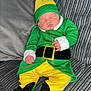 baby, child, sleeping, costume, elf, green_clothing, yellow_clothing, hat, couch, pillow, indoor, infant, cute, resting, soft_fabric, home, person, portrait, cozy, holiday