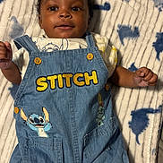 Princeton is registered to the contest to win money with this photo: baby, infant, denim_overalls, stitch, cartoon, blanket, patterned_blanket, smiling, cute, child, clothing, blue, fabric, button, portrait, young_child, lying_down, indoor, soft_texture, happy