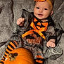 baby, child, pumpkin, halloween_costume, orange, black, striped_tights, headband, bow, smile, happy, blanket, cute, festive, holiday, sitting, face, person, infant, cozy