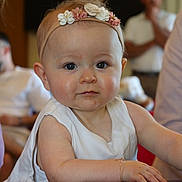 Arya participe au concours pour gagner de l'argent avec cette photo : baby, child, infant, headband, flower, bracelet, table, white_clothing, face, eyes, skin, arm, hand, person, indoor, blurred_background, adult, focus, portrait, curious