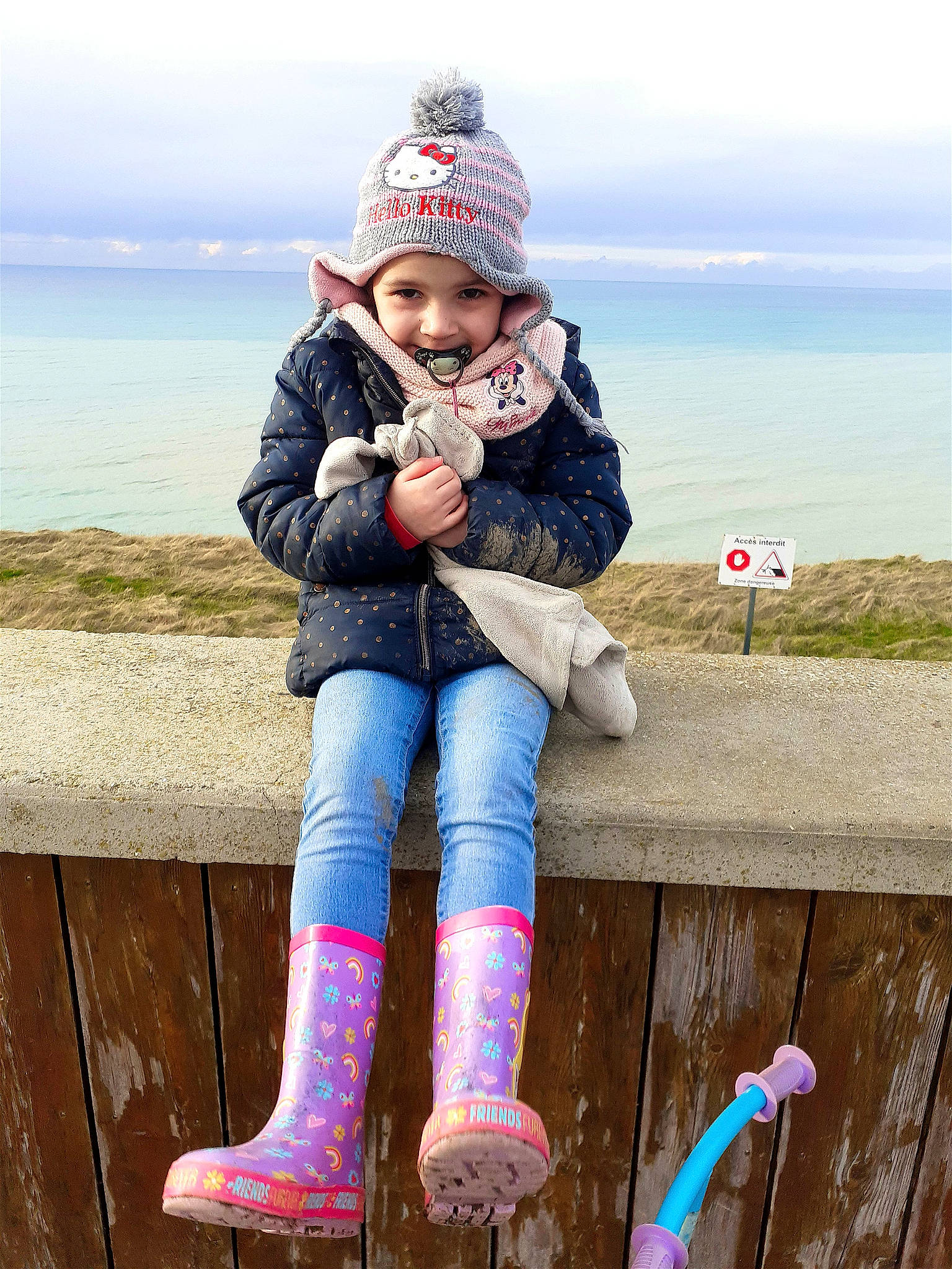 Mia a rejoint le concours — aidez-le/la à gagner de superbes lots ! cap, eye, face, fun, happy, headwear, human_leg, jacket, joy, knee, lake, leisure, outerwear, people_in_nature, person, sitting, sky, smile, thigh, toddler