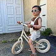 Noah participe au concours pour gagner de l'argent avec cette photo : toddler, child, balance_bike, sunglasses, overalls, sneakers, outdoor, concrete, door, wall, plant, summer, casual, fashion, young_child, play, portrait, side_view, cool, confident