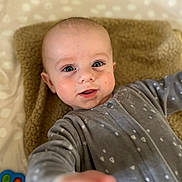 Roméo a rejoint le concours — aidez-le/la à gagner de superbes lots ! baby, infant, child, onesie, gray_clothing, blanket, toy, blue, orange, pink, green, face, hand, smiling, curious, lying_down, indoor, closeup, soft_texture, cute
