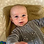 baby, infant, child, onesie, gray_clothing, blanket, toy, blue, orange, pink, green, face, hand, smiling, curious, lying_down, indoor, closeup, soft_texture, cute