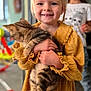 Emy a rejoint le concours — aidez-le/la à gagner de superbes lots ! child, kitten, cat, blonde_hair, yellow_dress, smiling, indoor, person, holding, pet, young_child, happy, portrait, blurred_background, floor, furniture, home, cute, playful, family