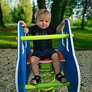 Ayden participe au concours pour gagner de l'argent avec cette photo : blonde_hair, blue_handles, child, daylight, grass, green_spring, nature, outdoor, pebbles, person, playground, sand, sandals, shirt, shorts, smile, spring_rocker, sunlight, toddler, trees