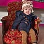 Ayden a rejoint le concours — aidez-le/la à gagner de superbes lots ! armchair, brown_pants, chair, child, coat, festive_garland, floor, footwear, happy, hat, indoor, knit_hat, patterned_fabric, person, portrait, smile, toddler, vintage_furniture, warm_clothing, wooden_armrest