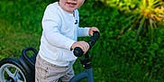 Ayden a rejoint le concours — aidez-le/la à gagner de superbes lots ! balance_bike, bike, casual_clothing, child, daylight, fun, grass, greenery, happy, nature, outdoor, person, play, shorts, smile, sneakers, toddler, toy, white_jacket, young