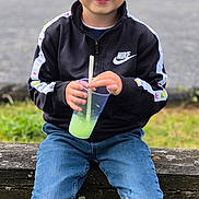 Ayden participe au concours pour gagner de l'argent avec cette photo : child, boy, smiling, outdoor, bench, grass, jeans, jacket, nike, drink, plastic_cup, straw, sneakers, casual_clothing, daylight, portrait, young, happy, nature, seated