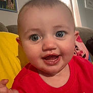 Kylee joined the competition — help win amazing prizes! baby, child, face, smile, red_shirt, blue_eyes, close_up, indoor, couch, cushion, hand, person, portrait, furniture, home, happy, infant, young_child, living_room, cute
