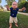 arms_outstretched, baby, barefoot, blue_shirt, bow_tie, bubble_chasing, bubbles, child, face, grass, lawn, outdoor, portrait, residential_background, shorts, smiling, standing, toddler, trees, walking