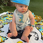 Louka a rejoint le concours — aidez-le/la à gagner de superbes lots ! baby, bib, blanket, blue_cap, child, colorful_ball, curious, cute, daylight, foot, grass, hand, outdoor, playful, sitting, striped_cap, summer, toy, tree, wooden_fence