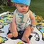 baby, bib, blanket, blue_cap, child, colorful_ball, curious, cute, daylight, foot, grass, hand, outdoor, playful, sitting, striped_cap, summer, toy, tree, wooden_fence