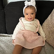 Tasnim participe au concours pour gagner de l'argent avec cette photo : baby, child, smiling, headband, bow, pink_dress, sitting, couch, pillow, soft_texture, indoor, happy, cute, person, portrait, infant, clothing, face, legs, foot