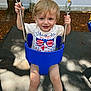 4th_of_july, blonde_hair, blue_swing, child, fence, fun, happy, holding, mat, outdoor, person, playground, shadow, smiling, summer, swing, toddler, tree, white_tshirt, yellow_chain