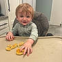 Anthony is registered to the contest to win money with this photo: appliance, cabinet, child, clothing, face, food, hair, hand, happy, high_chair, hoodie, indoor, kitchen, person, smiling, table, tile_floor, toddler, tray, waffle