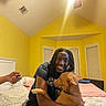 Rya joined the competition — help win amazing prizes! person, dog, hugging, smiling, bedroom, bed, cuddle, pet, affection, indoors, yellow_walls, portrait, black_shirt, long_hair, dog_collar, brown_dog, bed linens, window, dresser, remote_control