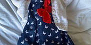 Ida is registered to the contest to win money with this photo: baby, bed, blanket, butterfly_pattern, child, clothing, cute, dress, hands_up, indoor, infant, newborn, peaceful, portrait, red_bow, resting, sleeping, soft_texture, tights, white_cardigan