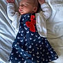 baby, bed, blanket, butterfly_pattern, child, clothing, cute, dress, hands_up, indoor, infant, newborn, peaceful, portrait, red_bow, resting, sleeping, soft_texture, tights, white_cardigan