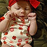 newborn, baby, infant, sleeping, portrait, close_up, red_bow, headband, onesie, ladybugs, flowers, patterned_clothing, fists, hands, face, indoors, blanket, camouflage, sitting, peaceful