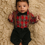 Dakari joined the competition — help win amazing prizes! baby, infant, plaid_shirt, bow_tie, suspenders, black_pants, barefoot, curly_hair, lying_down, fluffy_rug, soft_texture, indoors, portrait, cute, child, young, fashion, casual, closeup, relaxed