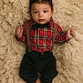 baby, infant, plaid_shirt, bow_tie, suspenders, black_pants, barefoot, curly_hair, lying_down, fluffy_rug, soft_texture, indoors, portrait, cute, child, young, fashion, casual, closeup, relaxed