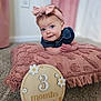 baby, infant, headband, pink, pillow, carpet, sign, wooden_sign, flower, 3_months, closeup, portrait, cute, child, indoor, smiling, face, clothing, decor, soft