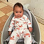 baby, infant, onesie, crab_pattern, baby_seat, indoor, tiled_floor, wall, child, cute, relaxed, looking_at_camera, small_child, seat, mesh, gray, white_clothing, orange, playful_pattern, casual
