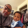 child, baby, infant, adult, man, father, portrait, selfie, indoors, bedroom, clothing, closet, eyepatch, leopard_print, bib, blue_shirt, curly_hair, serious, family, photography