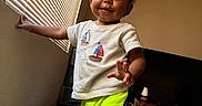 Kobe joined the competition — help win amazing prizes! toddler, child, boy, smiling, standing, portrait, indoors, living_room, window, blinds, television, furniture, clothing, t_shirt, shorts, neon, blanket, rug, home, happy