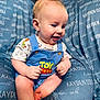 baby, child, romper, toy_story, blue_clothing, cushion, personalized, text, smiling, sitting, indoor, cute, infant, foot, hand, face, head, person, comfort, soft_furniture