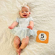 Jessica joined the competition — help win amazing prizes! baby, infant, smiling, headband, bow, milestone_card, five_months, blue_dress, lying_down, blanket, textured_blanket, cute, happy, child, human, portrait, indoor, infant_fashion, baby_photography, celebration