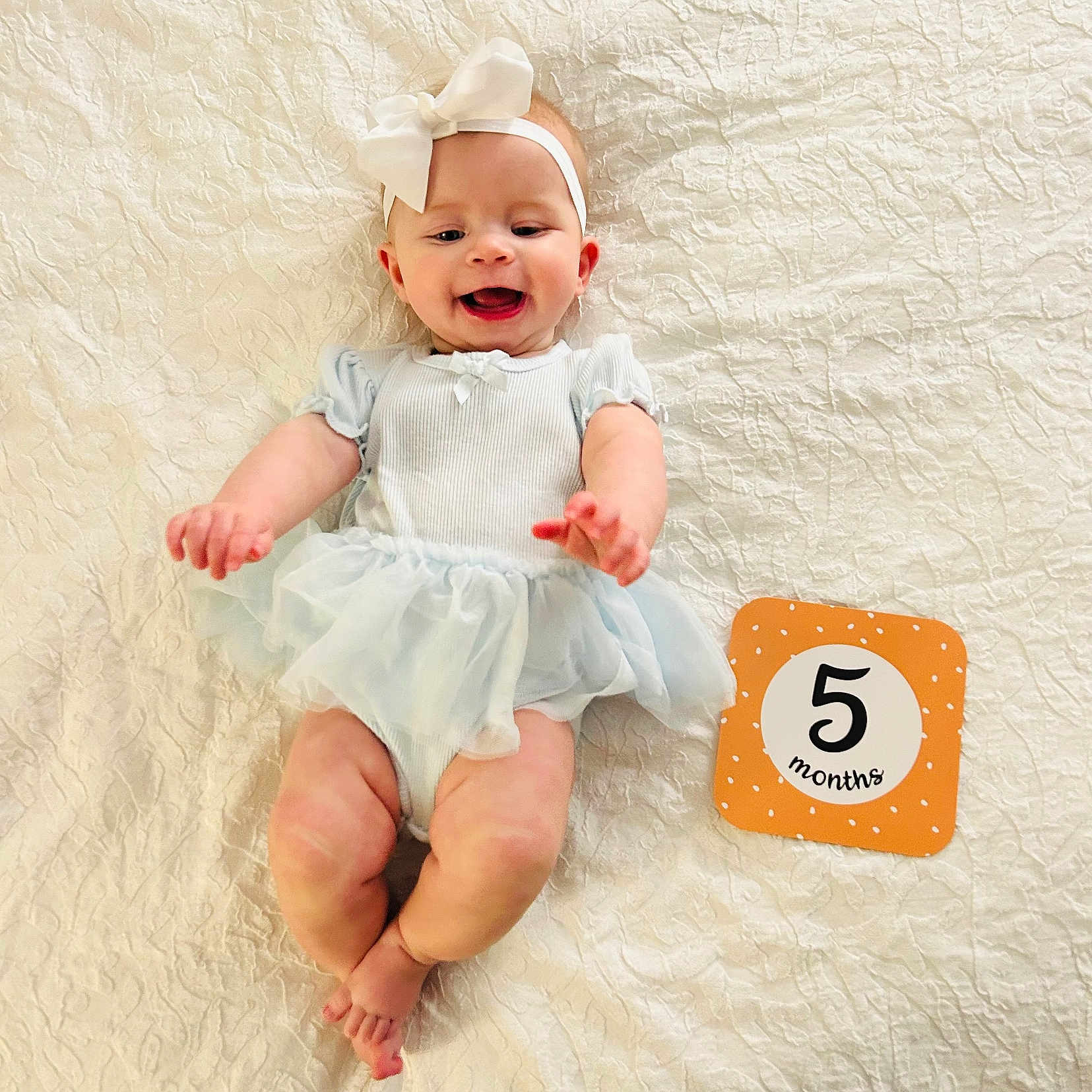 Jessica joined the competition — help win amazing prizes! baby, infant, smiling, headband, bow, milestone_card, five_months, blue_dress, lying_down, blanket, textured_blanket, cute, happy, child, human, portrait, indoor, infant_fashion, baby_photography, celebration