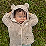 baby, child, hoodie, bear_ears, grass, outdoor, cute, smile, face, clothing, nature, greenery, portrait, cozy, infant, lying_down, casual, playful, young_child, cute_expression