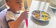 Kayden participe au concours pour gagner de l'argent avec cette photo : child, curious, curly_hair, daylight, eating, food, fork, french_fries, high_chair, home, indoor, kitchen, meal, person, plate, seat, shirt, table, toddler, window