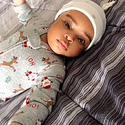 Zain is registered to the contest to win money with this photo: baby, infant, pajamas, hat, bed, striped_bedspread, lying_down, face, hands, cute, child, indoors, sleepwear, festive_clothing, reindeer, santa_claus, expression, portrait, cozy, soft_lighting