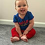 baby, barefoot, blue_shirt, carpet, child, chubby_cheeks, cute, floor, happy, indoor, infant, person, playful, portrait, red_pants, sitting, smiling, tongue_out, wall, young_child