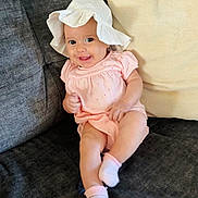 Genevieve is registered to the contest to win money with this photo: baby, infant, smiling, hat, socks, couch, pillow, clothing, indoor, cute, child, person, happy, seated, face, skin, young, comfort, fabric, home