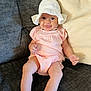 Genevieve is registered to the contest to win money with this photo: baby, child, infant, smile, hat, white_hat, pink_outfit, couch, pillow, indoors, happy, sitting, cute, sock, face, person, young_child, cozy, comfortable, portrait