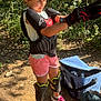 child, girl, protective_gear, elbow_pads, knee_pads, gloves, headband, shorts, sneakers, outdoor, nature, greenery, sunlight, dirt_ground, bag, bottle, sportswear, preparation, activity, ready