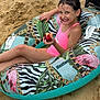 child, girl, beach, sand, inflatable_tube, swimsuit, pink, fruit, peach, smile, summer, vacation, outdoor, relaxing, happy, water_toy, footwear, towel, playful, nature