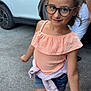 child, girl, glasses, outdoor, street, car, white_car, denim_shorts, peach_top, hair_tie, walking, sidewalk, casual_clothing, person, summer, footwear, smiling, happy, daylight, urban
