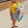 child, girl, sunglasses, yellow_tshirt, stitch_character, shopping_bag, shorts, flip_flops, smiling, outdoor, sunlight, shadow, pavement, railing, parked_cars, casual_clothing, happy, standing, summer, hair_tied