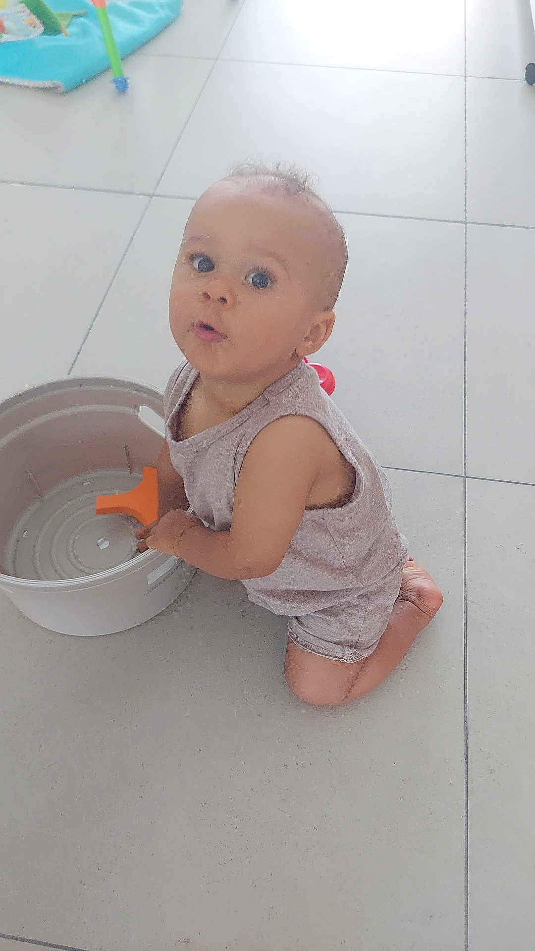 Aaron a rejoint le concours — aidez-le/la à gagner de superbes lots ! child, toddler, indoor, floor, tile, bucket, toy, plastic, curious, kneeling, clothing, shorts, sleeveless_shirt, person, skin, baby, expression, play, home, light